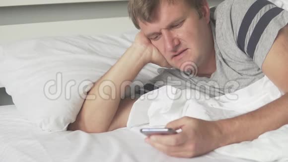 一个拿着手机的男人早上躺在床上检查视频的预览图
