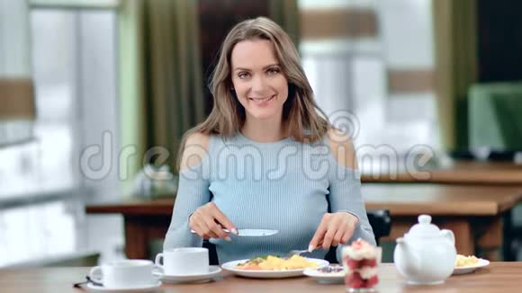 微笑的女人在咖啡桌上摆姿势吃新鲜美味食物的肖像中型摄影机视频的预览图