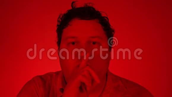 用红色灯光拍摄的肖像男人在看镜头时做沉默的手势视频的预览图