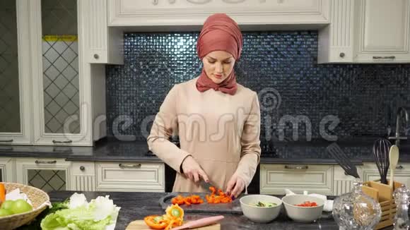 戴头巾的女人站在厨房的桌子上切菜视频的预览图