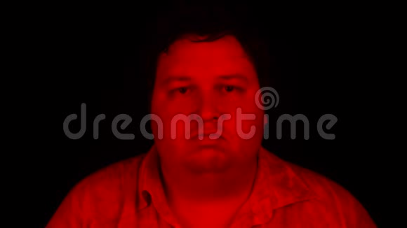 用红色灯光拍摄的肖像胖子站在黑色背景上看着摄像机视频的预览图
