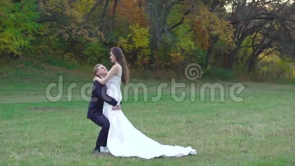 年轻的新郎在一个秋天公园的中央旋转着迷人的新娘美丽的风景中新婚快乐视频的预览图