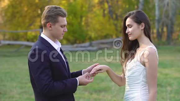 秋天公园阳光明媚的新郎把漂亮的戒指戴在新娘的手指上视频的预览图