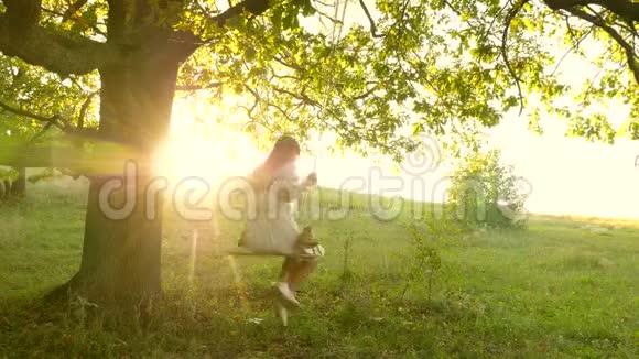 年轻女孩在阳光下在橡树枝上荡秋千飞行的梦想快乐的童年概念一个漂亮的女孩视频的预览图