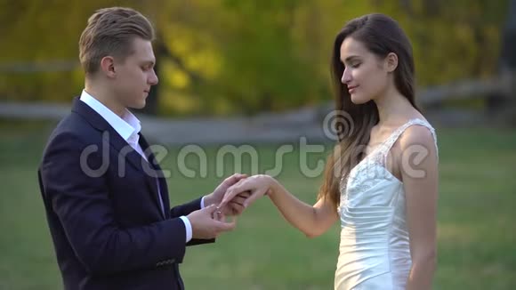 新郎把漂亮的戒指戴在新娘的手指上在秋天公园的阳光下亲吻她的手视频的预览图