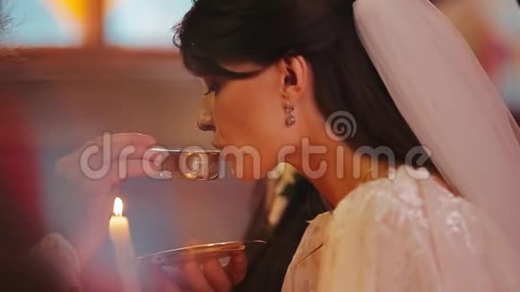 美丽的新娘穿着豪华的白色连衣裙在牧师手中的镀金杯中喝着神圣的水基督教传统视频的预览图