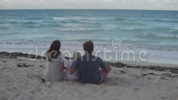 一家人背着镜头坐在海边的沙滩上视频的预览图