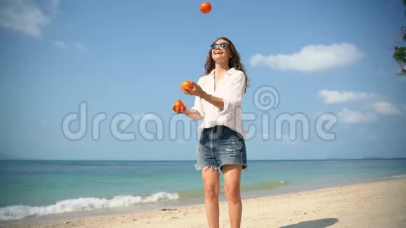 阳光明媚的一天年轻开朗的女人在海滩上摆弄橘子视频的预览图