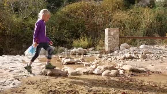 一个孩子在石头上横过小溪脚也没有弄湿视频的预览图