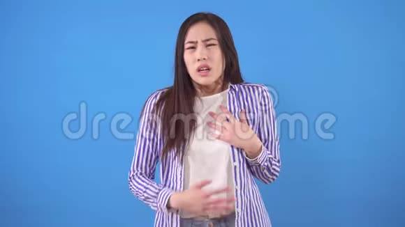 带着心痛的年轻亚洲女人站在蓝色的背景上视频的预览图