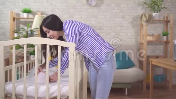 婴儿床旁边一位积极的亚洲年轻妈妈的肖像视频的预览图