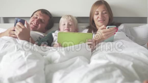一家人带着孩子躺在床上床上有平板电脑和手机视频的预览图