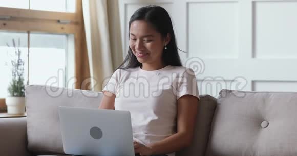 微笑的亚洲年轻女性在家中使用笔记本电脑在线聊天视频的预览图