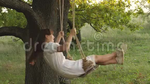 自由女孩在阳光下在橡树枝上荡秋千飞行的梦想快乐的童年概念一个漂亮的女孩视频的预览图
