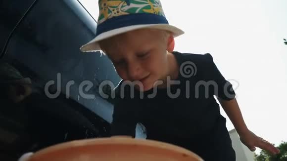 戴帽子的小男孩用肥皂和海绵洗一辆车视频的预览图