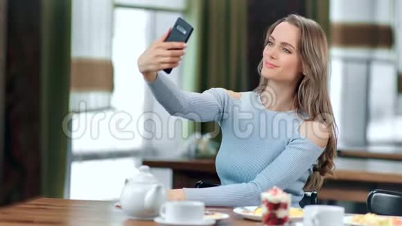 微笑美丽的年轻女子自拍使用智能手机摆姿势在咖啡馆4k龙红相机视频的预览图