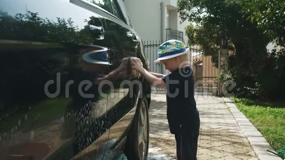 戴帽子的小男孩用肥皂和海绵洗一辆车视频的预览图