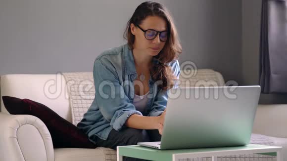 一位年轻女子手提电脑坐在沙发上举行在线咨询视频的预览图