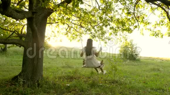 自由女孩在阳光下在橡树枝上荡秋千飞行的梦想快乐的童年概念一个漂亮的女孩视频的预览图