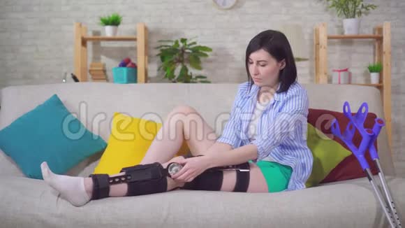 不满意的年轻女子受伤后膝盖弯曲膝盖支撑在家里的沙发上视频的预览图