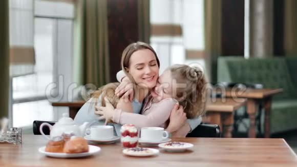 可爱的母亲拥抱可爱的女儿在咖啡馆的早餐桌感受爱中型摄影机视频的预览图