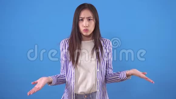 困惑和愤怒的年轻亚洲女人站在蓝色的背景上视频的预览图