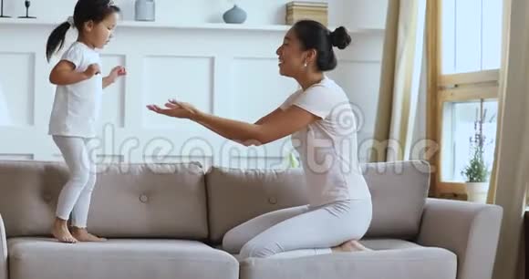 可爱的亚洲小女孩在沙发上跳着跟妈妈玩视频的预览图