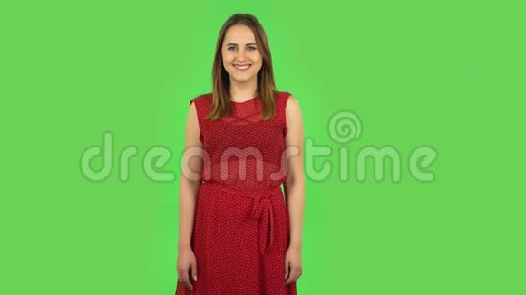 穿着红色衣服的温柔女孩正微笑着看着相机交叉着她的手臂放在胸前绿色屏幕视频的预览图
