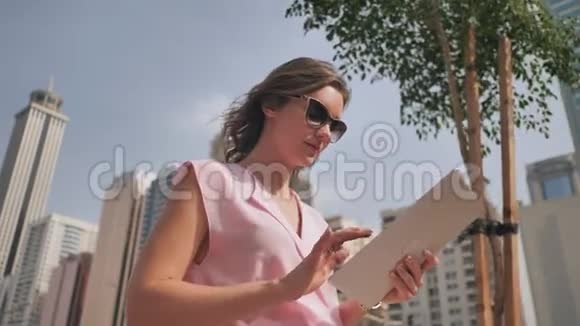 一个女孩在大都市摩天大楼背景下的平板电脑上工作视频的预览图
