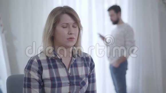 年轻漂亮的白种人妻子仔细地听着丈夫在后台打电话嫉妒的肖像视频的预览图