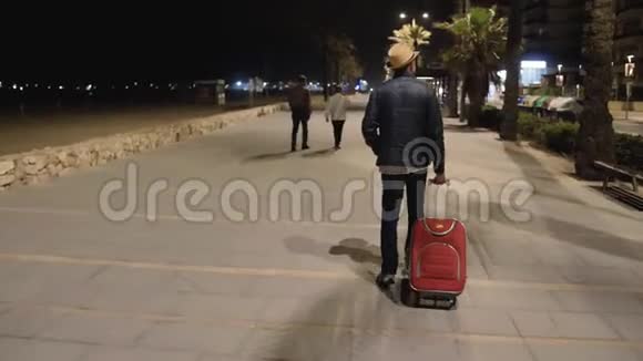 一个带着红色手提箱的旅行者晚上沿着长廊散步休息了视频的预览图