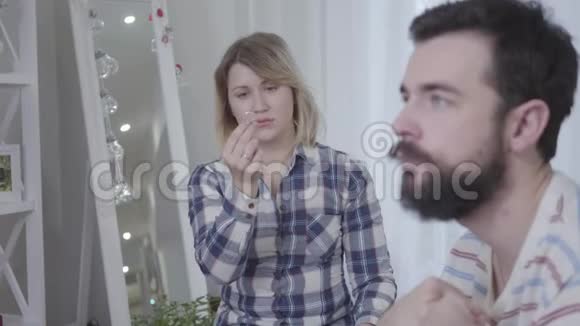 沮丧的年轻女人看着手中的结婚戒指和坐在前台的模糊丈夫的肖像压力视频的预览图