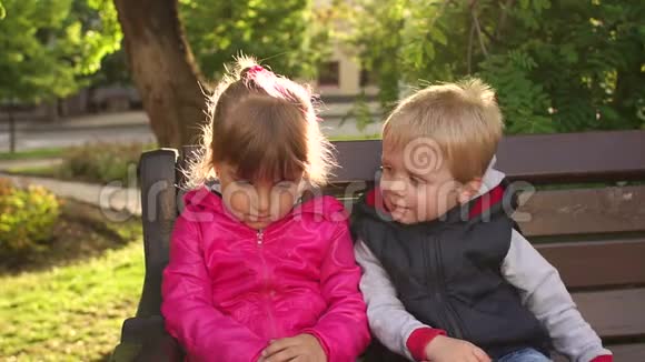小男孩在公园长椅上亲吻悲伤的小女孩视频的预览图