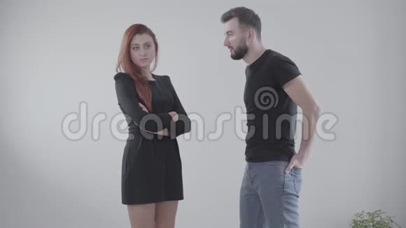 年轻英俊的白种人男人和愤怒的红发女人站在白色背景下争吵穿着优雅的女孩视频的预览图