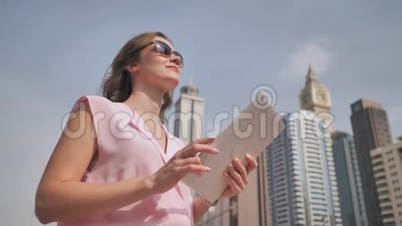 一个欧洲貌美的女孩在迪拜摩天大楼的背景上用平板电脑工作视频的预览图