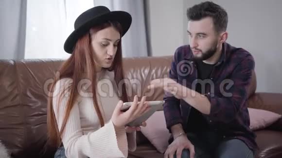 年轻可爱的高加索女人作为她的丈夫或男朋友解释如何使用平板电脑戴帽子的优雅女孩视频的预览图