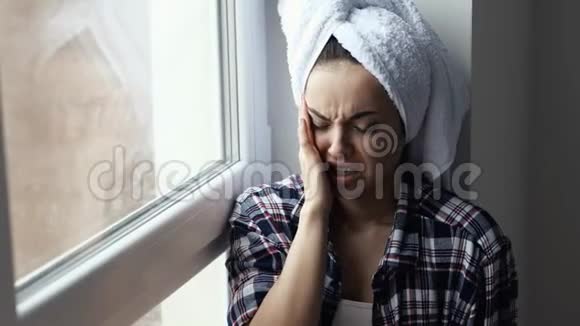 年轻女子在检疫期间呆在家里洗澡或淋浴后坐在窗前打喷嚏成白色组织喝视频的预览图