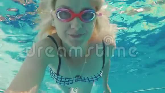 一位年轻女子在水下拍摄视频漂浮在水池里用眼镜看着摄像机视频的预览图