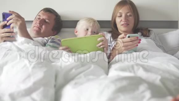 一家人早上在床上使用手机手机和平板电脑视频的预览图