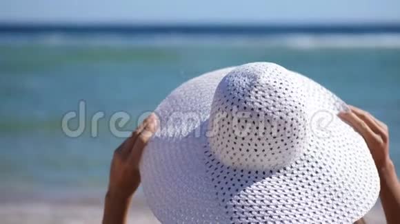 特写镜头模糊的水背景戴着白色大帽子的年轻女人坐在海边戴着她的帽子有文字的地方视频的预览图