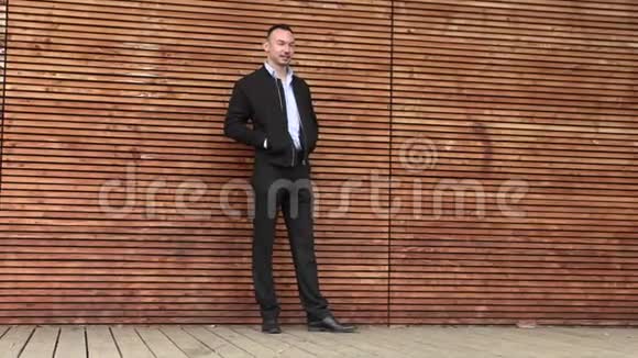 一个穿黑色夹克的人靠在木墙上视频的预览图