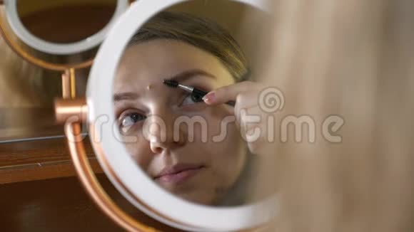 年轻漂亮的女人照镜子用化妆品画眉毛视频的预览图