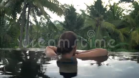 在热带花园的水池里休息的年轻女子视频的预览图