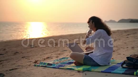 一位年轻的女作家拿着笔记本电脑坐在海滩上打字视频的预览图