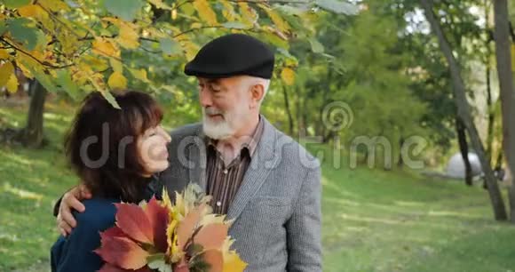 快乐的老人和女人带着一束叶子在阳光明媚的天气温暖舒适的公园里拥抱一对老夫妇视频的预览图