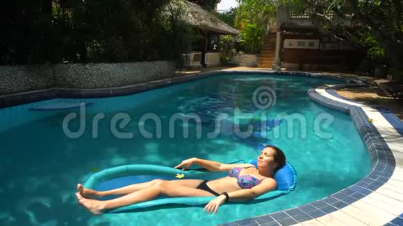 阳光明媚的一天年轻女子躺在游泳池里的水床垫上视频的预览图