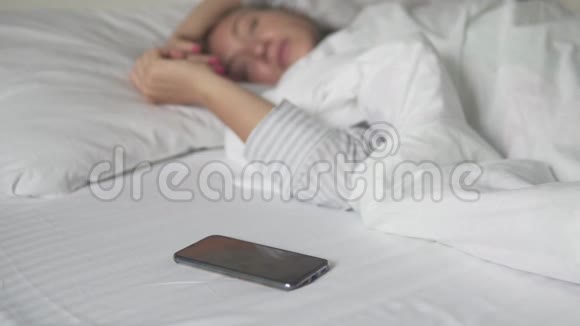 一个女人早上在床上关掉手机上的闹钟在电话的焦点上视频的预览图