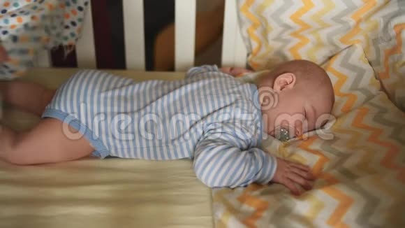 一个小孩子正睡在婴儿床上妈妈用毯子给婴儿盖上被子视频的预览图