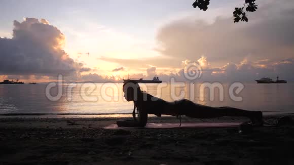 穿泳装的湿女人在日出时在海滩上做木板运动视频的预览图