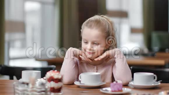 快乐可爱的女孩坐在桌子上看杯子和甜点中型近距离拍摄4k红色相机视频的预览图
